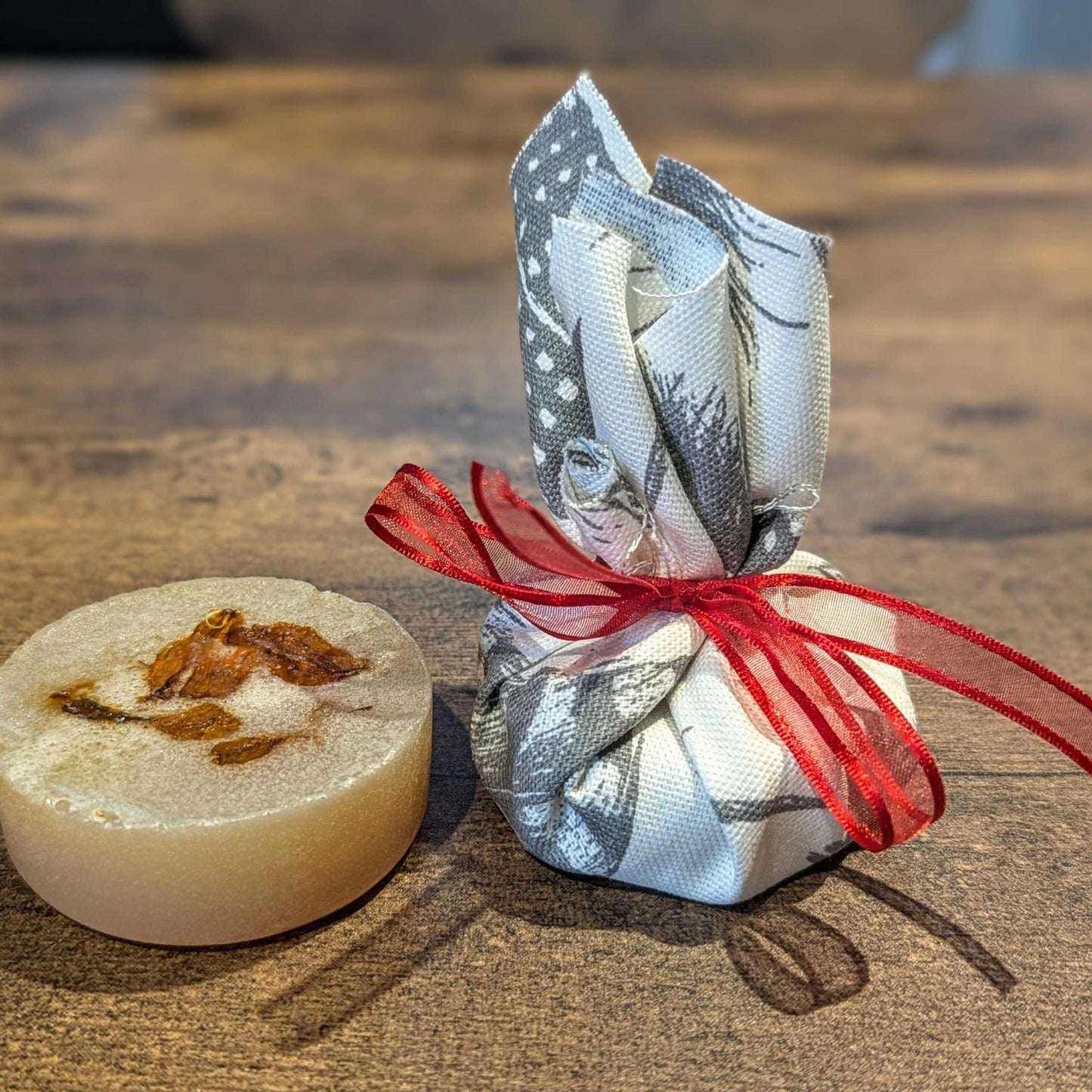Bar of soap with a wrapped product tied with red ribbon on a wooden surface