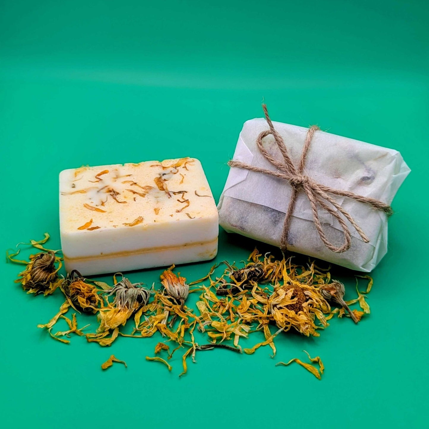 Two bars of soap, one unwrapped and one wrapped in paper with twine, on a green background.