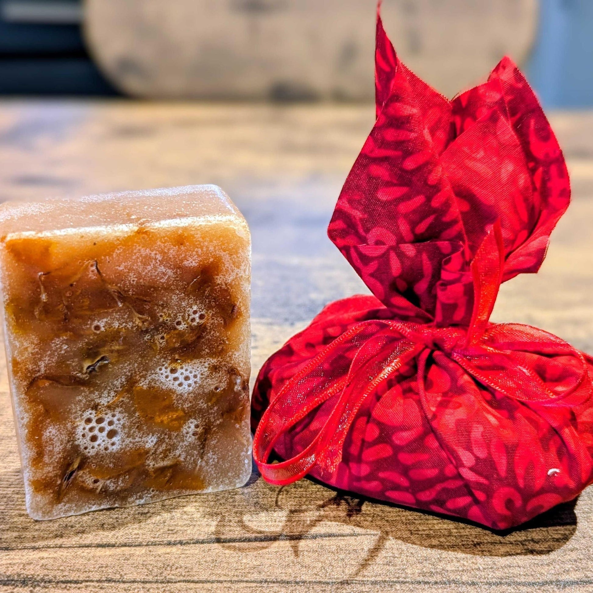 Bar of brown soap next to a red floral-patterned bag on a wooden surface