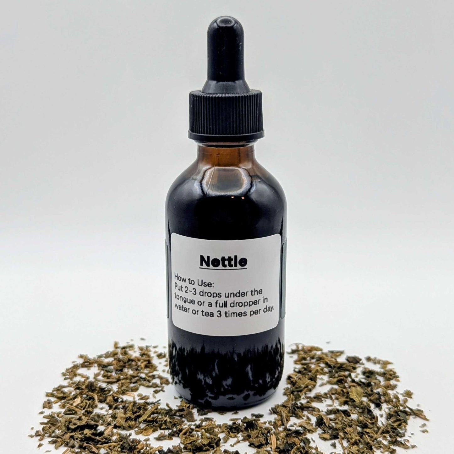Bottle of Nettle extract with dried nettle leaves on a white background
